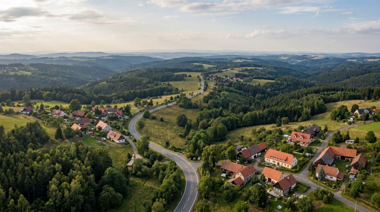 A realistic panoramic photograph showing the Erzgebirge and Bohemian border landscape with wooded hills, scattered villages, and a sense of the route leading toward Prague.