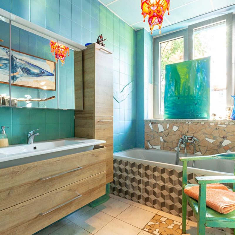 Kleines Badezimmer mit Badewanne und Duschmöglichkeit. Toilette und Pissoir befinden sich in einem separaten Raum direkt gegenüber.